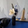 Petit bouquet de fleurs en papier dans un vase noir posé sur un bureau bleu, entouré d'un casque audio et d'une maquette Lego New York
