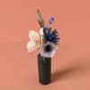 Petit bouquet de fleurs en papier d'art avec une hellébore ivoire, une anémone rose pâle, un chardon bleu, de la mini lavande et du mini olivier, dans un vase en bois sombre