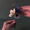 Bouquet de fleurs en papier tenu à deux mains, montrant la composition complète avec hellébore ivoire, anémone blanc et chardon bleu outremer