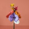 Main tenant un bouquet coloré de fleurs en papier : orchidée iris, renoncule, pavot corail, trèfle viola et ginkgo