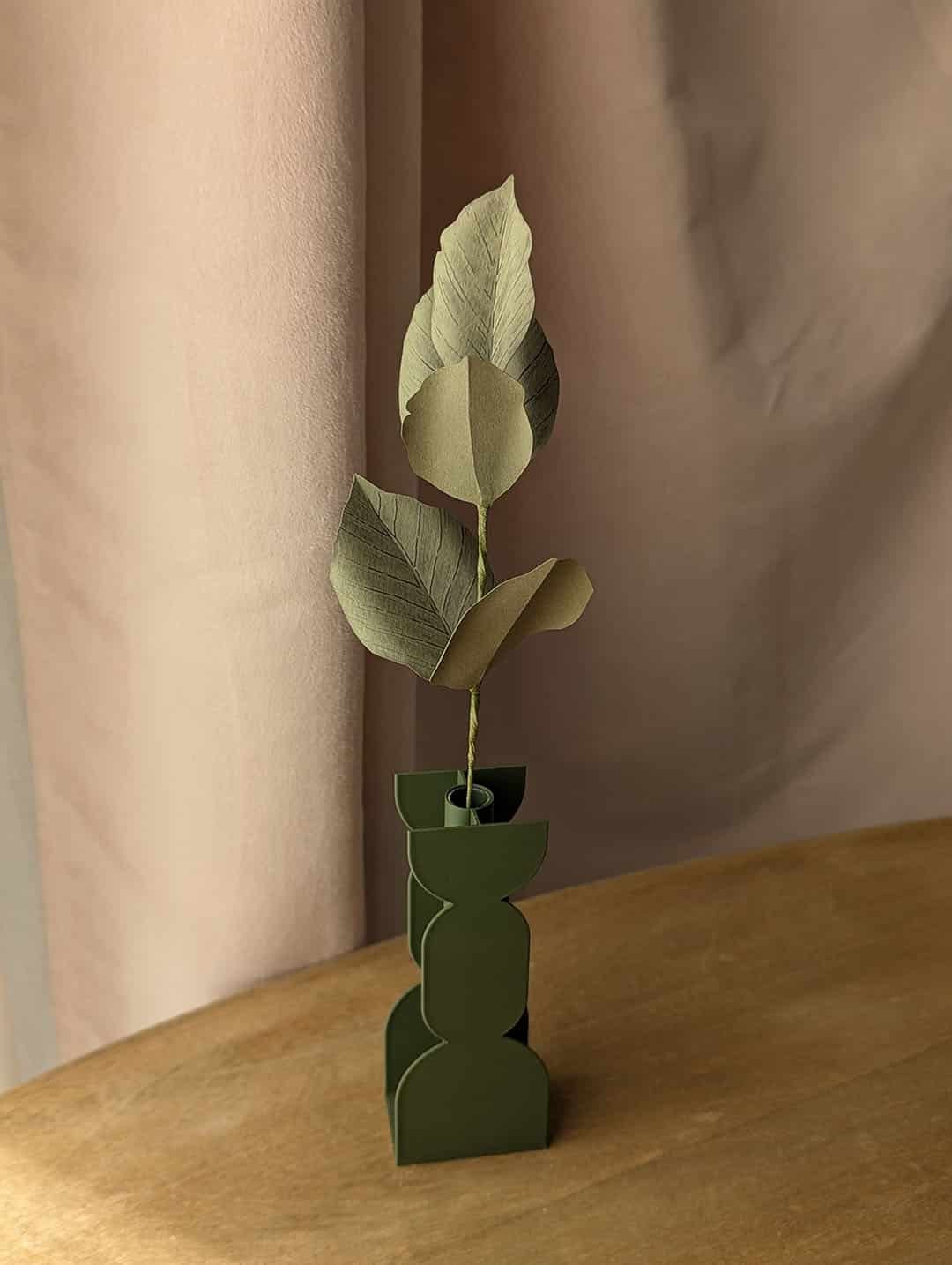Branche de hêtre en papier coloris vert olive dans un vase vert imprimé en 3D sur une table en bois