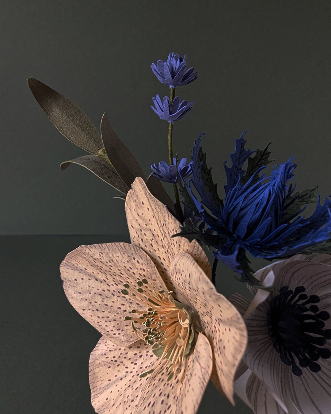 Gros plan sur une hellébore ivoire en papier avec ses étamines, aux côtés d'un mini chardon outremer et d'une mini lavande bleue