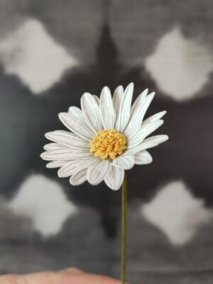 Gros plan sur une pâquerette en papier blanc faite main avec détails de pétales dessinés au trait noir.