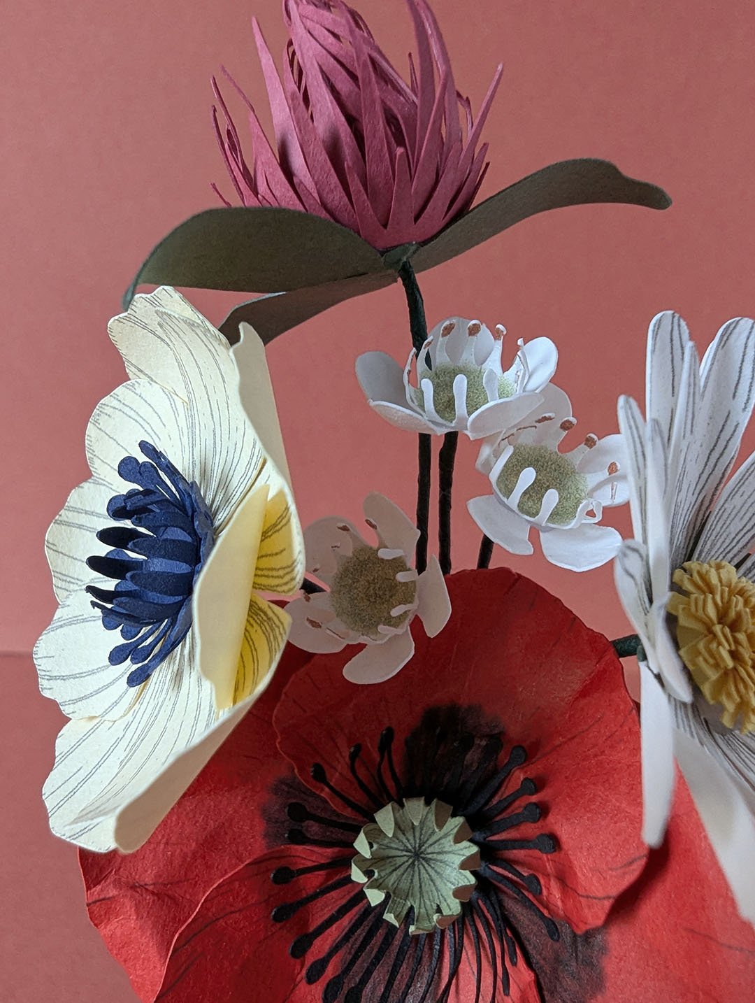Bouquet de fleurs en papier artisanal de face, composé d'un coquelicot rouge, d'une anémone crème, d'une marguerite blanche et d'un trèfle bordeaux