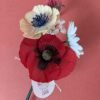 Bouquet de fleurs en papier artisanal tenu debout de biais, coquelicot rouge et anémone crème au premier plan, fond terracotta