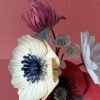 Bouquet de fleurs en papier artisanal avec coquelicot rouge, anémone crème à cœur bleu marine et trèfle bordeaux, fond rose terracotta