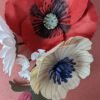 Vue plongeante sur un bouquet de fleurs en papier avec un petit coquelicot rouge et une anémone crème, sur fond terracotta