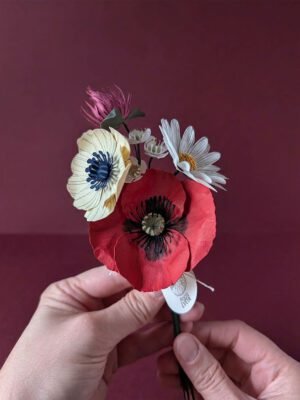 Bouquet de fleurs en papier artisanal tenu à deux mains, coquelicot rouge et anémone crème visibles, fond boredaux