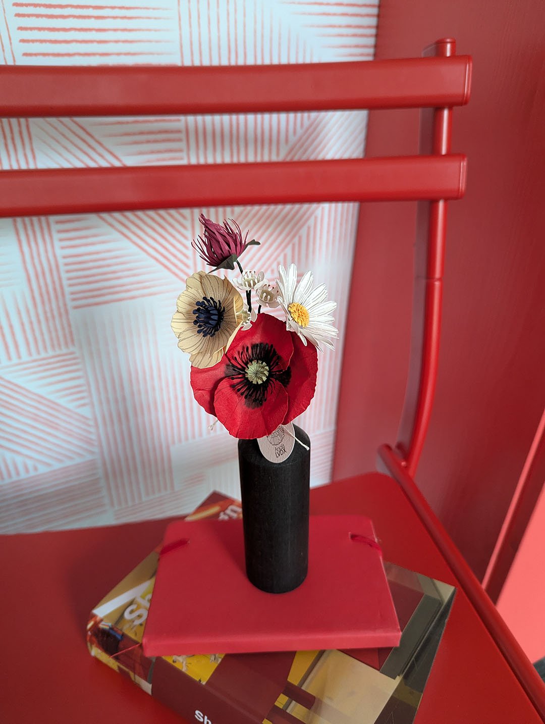Bouquet de fleurs en papier dans un vase noir, cadrage rapproché, chaise et papier peint rouge en arrière-plan, création Anaïs LVDX
