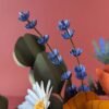 Gros plan sur deux tiges de lavande bleu violet et une pâquerette blanche au cœur jaune du bouquet Garrigue en fleurs de papier artisanales, fond rose