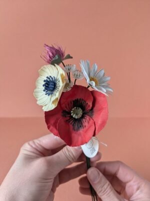 Mains tenant un bouquet de fleurs en papier : coquelicot, anémone ivoire, wax blanc, pâquerette et trèfle