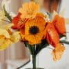 Vue rapprochée du bouquet Masterpiece Orange avec grande anémone jaune soleil au premier plan, pavots orange et iris bouton d'or, fleurs en papier artisanales