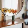 Bouquet de fleurs en papier Masterpiece Orange posé dans un vase vert kaki sur une commode vintage, avec reflet dans un miroir rond, décoration intérieure
