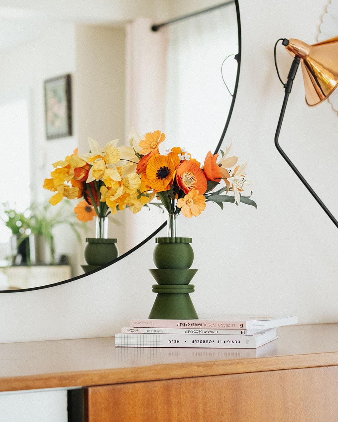 Double reflet du bouquet Masterpiece Orange dans un miroir rond, posé sur des livres sur une commode en bois, décoration intérieure artisanale