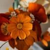Gros plan sur un cosmos coloris clémentine en papier crépon au cœur d'un bouquet artisanal, entouré de pavots et anémones, Anaïs LVDX