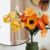 Bouquet de fleurs en papier Masterpiece Orange avec anémone jaune et iris bouton d'or dans un vase vert, fond miroir et rideau rose poudré