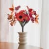 Bouquet de fleurs en papier d'art Masterpiece Rose dans un vase blanc géométrique sur fond blanc lumineux, pavots fuchsia et lys orange bien visibles