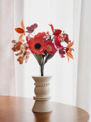 Bouquet de fleurs en papier d'art Masterpiece Rose dans un vase blanc géométrique sur fond blanc lumineux, pavots fuchsia et lys orange bien visibles