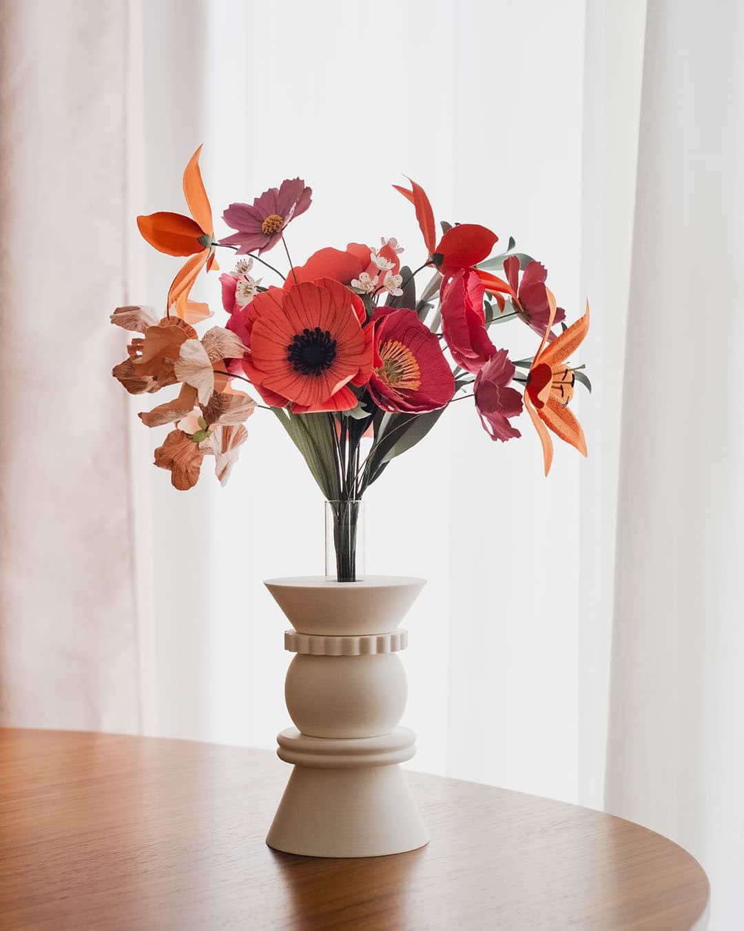 Bouquet de fleurs en papier d'art Masterpiece Rose dans un vase blanc géométrique sur fond blanc lumineux, pavots fuchsia et lys orange bien visibles