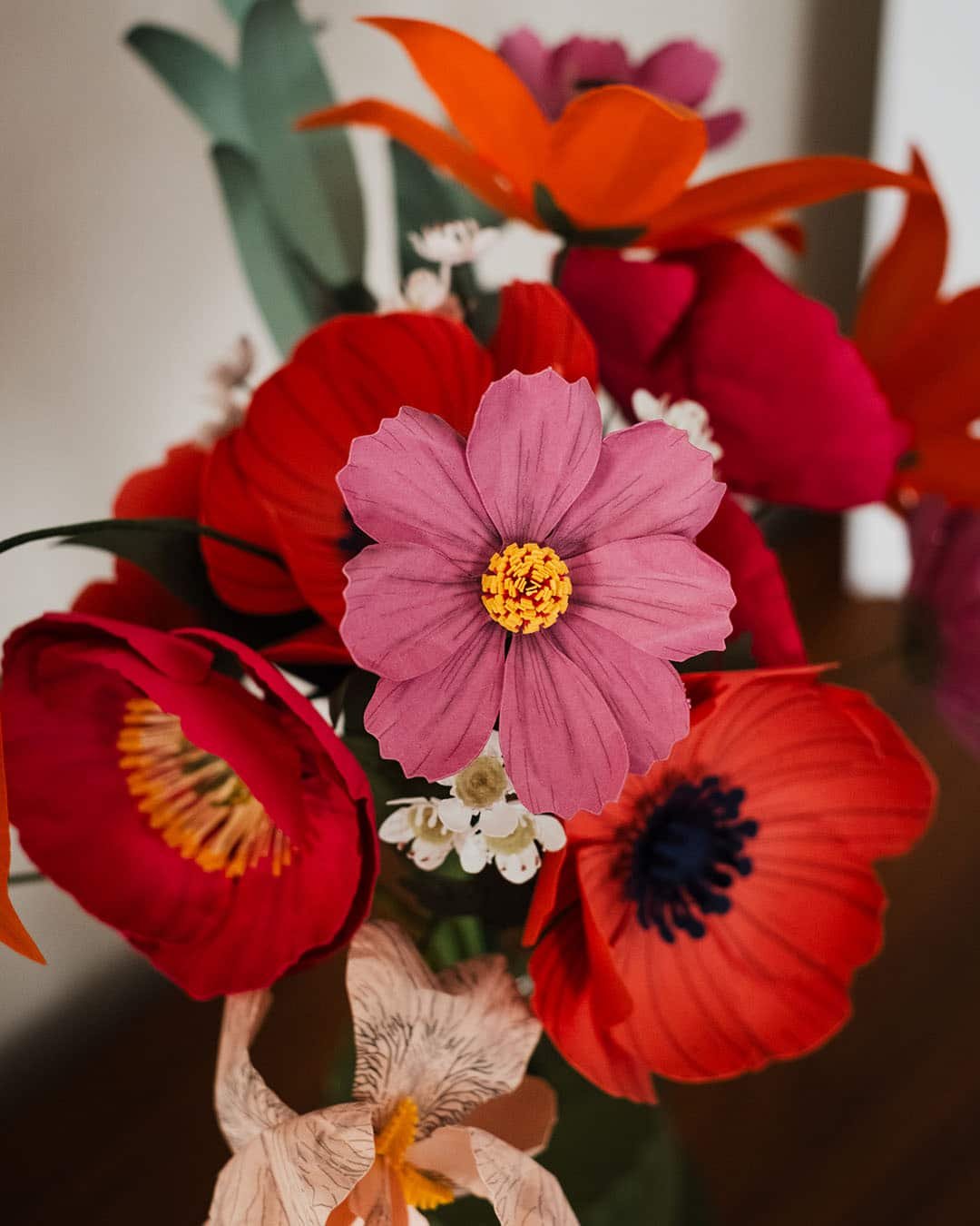 Gros plan sur un cosmos coloris hortensia en papier d'art teinté au centre du bouquet Masterpiece Rose, entouré d'anémones corail et pavots fuchsia, Anaïs LVDX