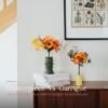 Comparaison de deux bouquets de fleurs en papier : le grand Masterpiece Orange dans un vase vert kaki et le plus petit Garrigue dans un vase jaune, sur une commode