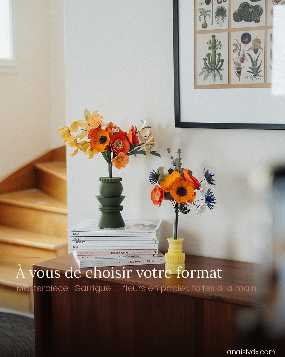 Deux bouquets artisanaux de fleurs en papier posés sur une commode : grand bouquet Masterpiece Orange dans un vase vert kaki et petit bouquet Garrigue dans un vase jaune, escalier en bois visible