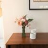 Bouquet de fleurs en papier Auguste dans un vase vert olive sur un buffet en bois, sous une planche botanique
