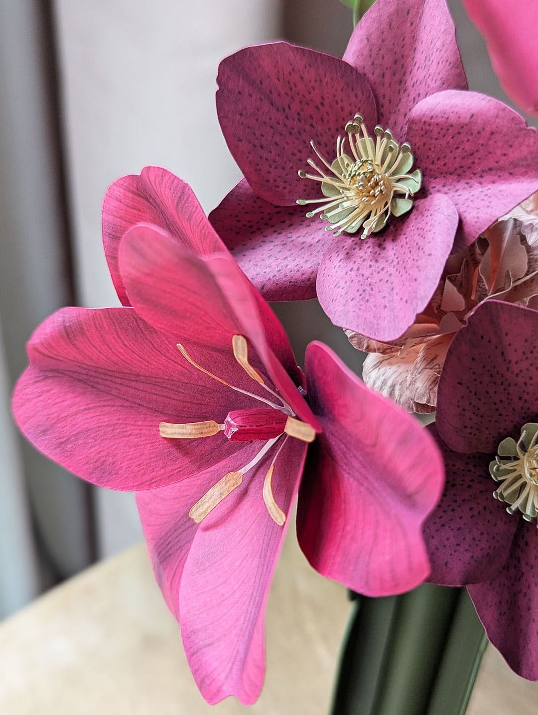 Gros plan sur une tulipe fuchsia ouverte et des hellébores viola en papier d'art, avec un œillet rosa au second plan