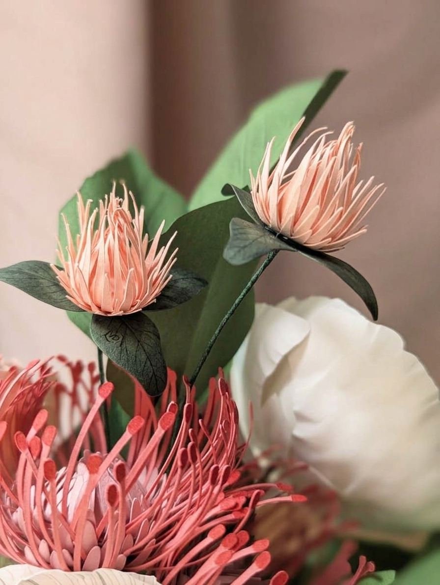Deux fleurs de trèfle rosa en papier d'art et leurs feuilles vertes, près d'un leucospermum et d'un pavot blanc