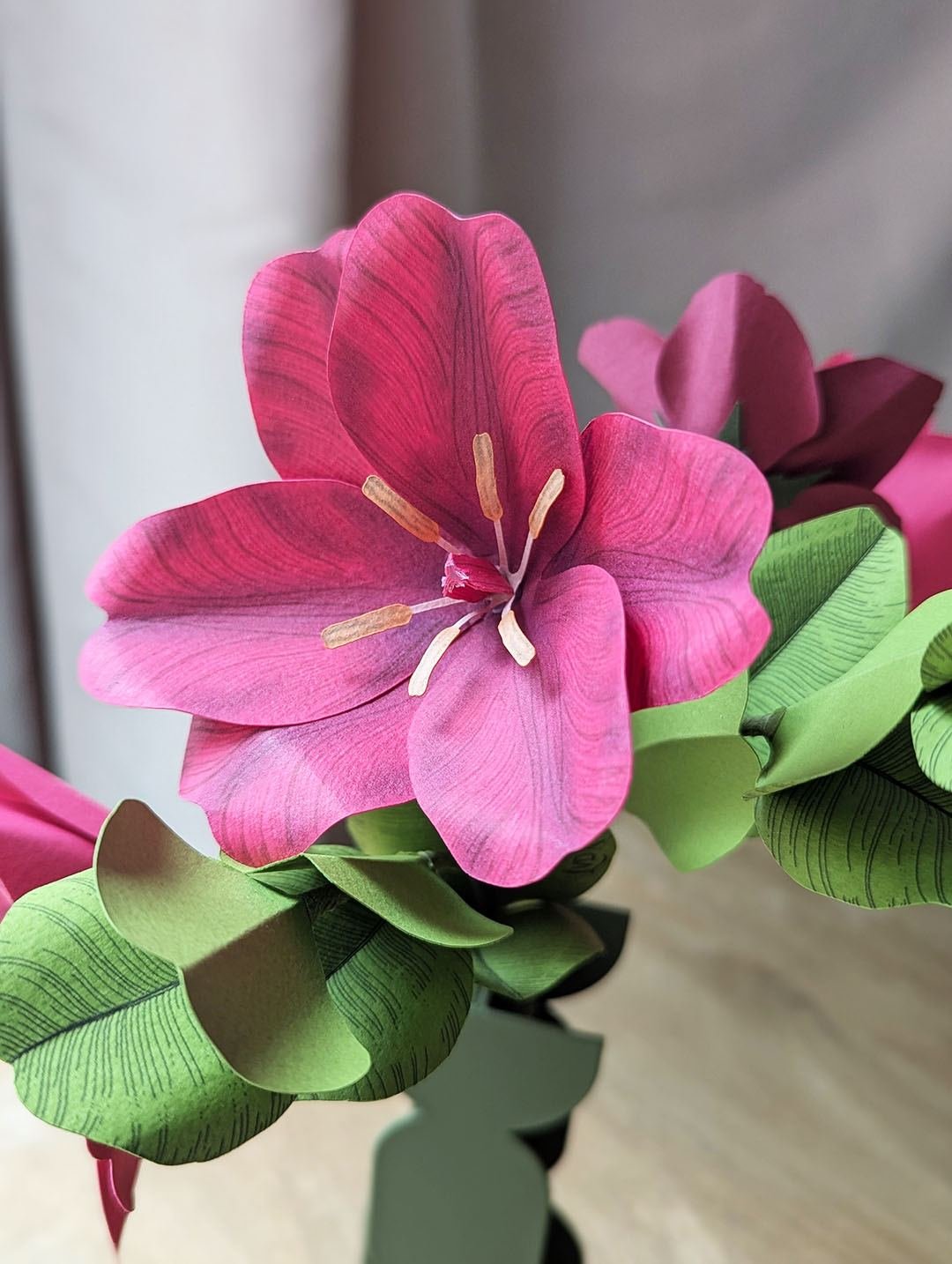 Tulipe fuchsia ouverte en papier d'art posée sur des feuilles de grand eucalyptus pistache, dans le bouquet Léo