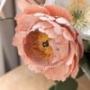 Gros plan sur une pivoine rosa en papier d'art avec étamines jaunes, à côté d'un pavot blanc
