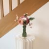 Bouquet de fleurs en papier dans un vase vert olive posé sur un socle en papier plissé devant un escalier en bois