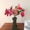 Bouquet de fleurs en papier avec tulipes fuchsia, hellébore viola et œillets rosa dans un vase vert olive, sur une table en bois