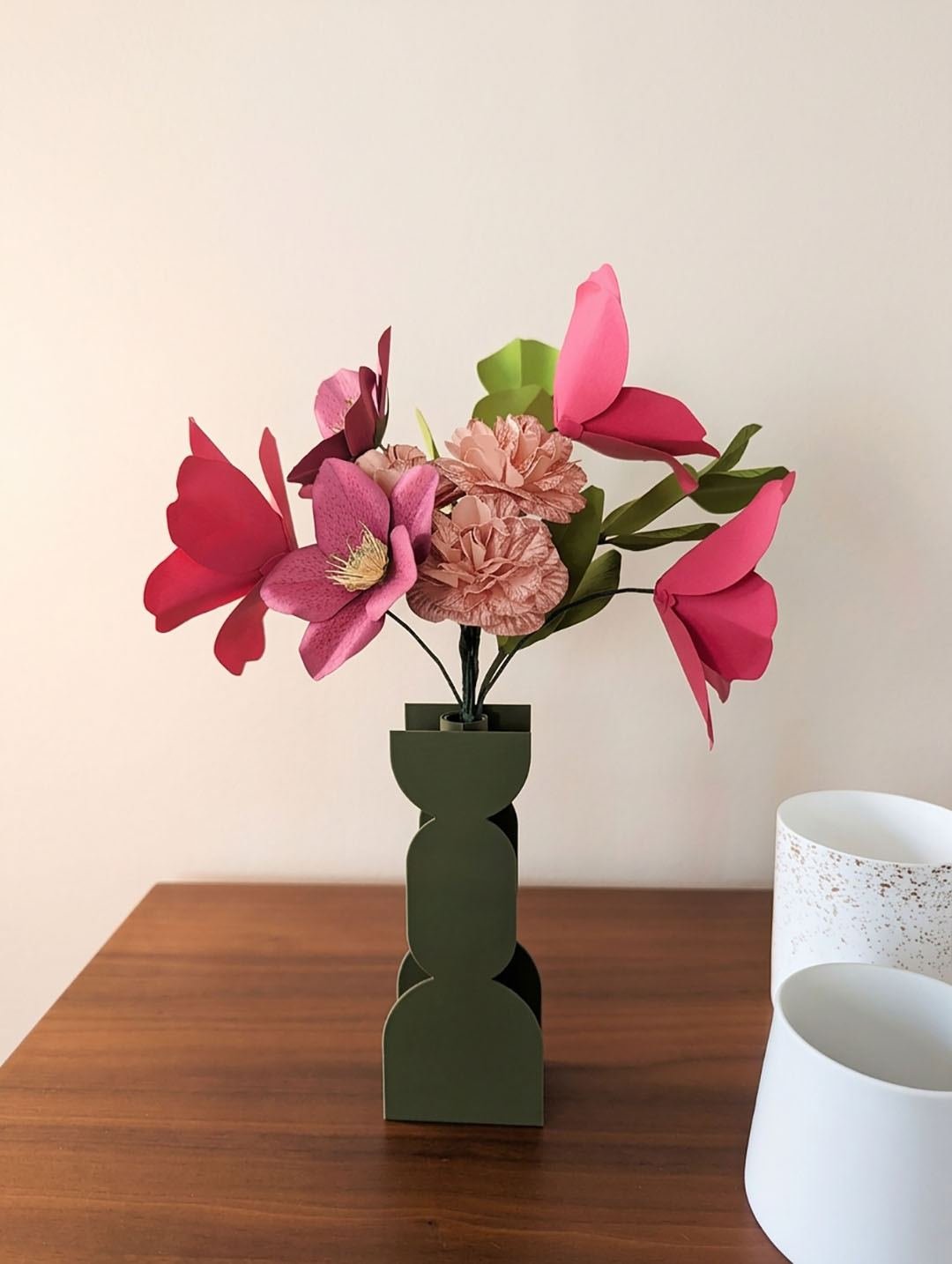Bouquet de fleurs en papier avec tulipes fuchsia, hellébore viola et œillets rosa dans un vase vert olive, sur une table en bois