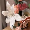 Gros plan sur un lys aurore blanc moucheté en papier d'art, entouré de pivoines et d'un pavot en papier