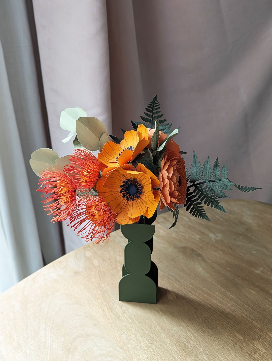 Vue d'ensemble du bouquet de fleurs en papier Théodore avec anémones, renoncules, leucospermums et fougères dans un vase vert