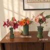 Trois bouquets de fleurs en papier Léo, Théodore et Auguste dans des vases vert olive sur un buffet en noyer