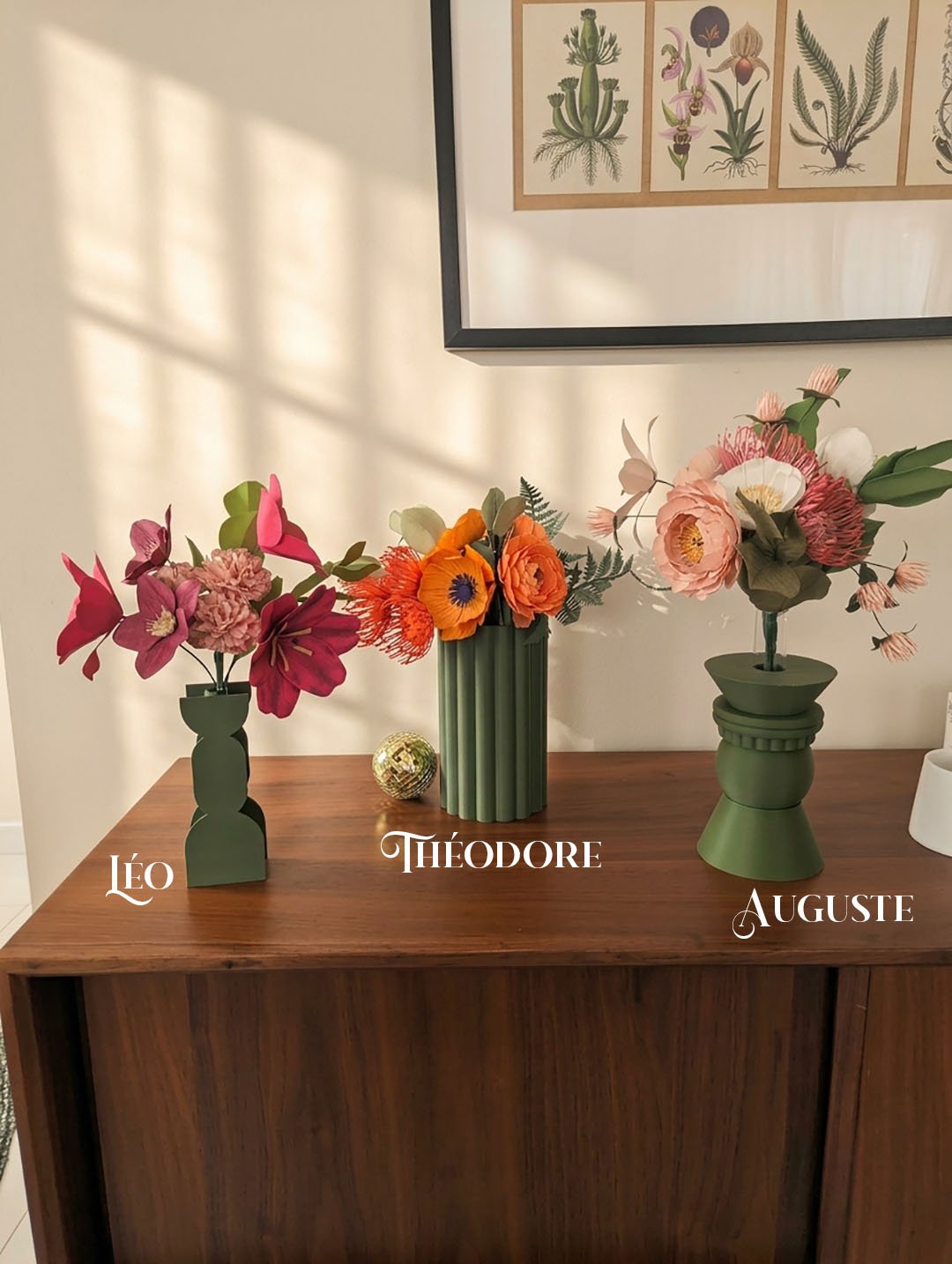 Trois bouquets de fleurs en papier Léo, Théodore et Auguste dans des vases vert olive sur un buffet en noyer