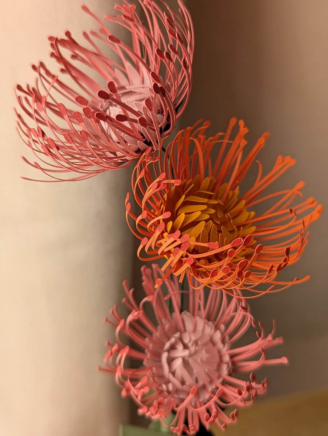 Gros plan sur trois têtes d'épingles en papier, orange et rose, aux étamines déployées