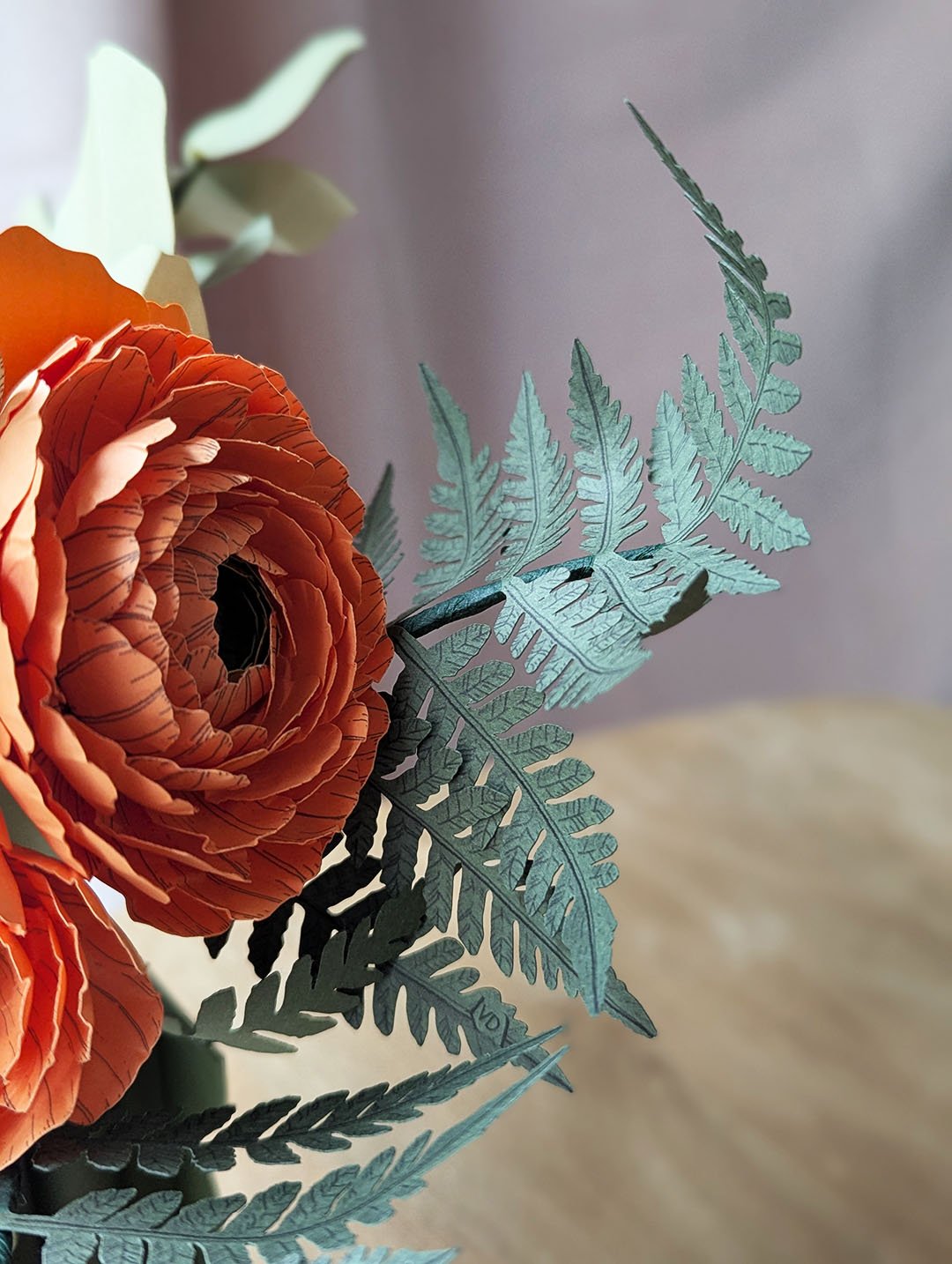 Fougère vert océan en papier d'art à côté d'une renoncule Clémentine, détail du bouquet de fleurs en papier Théodore