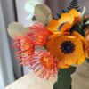 Gros plan sur trois leucospermums orange et deux anémones jaune soleil en papier d'art avec eucalyptus vert tilleul