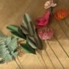 Sélection de fleurs et feuillages en papier posés sur bois, fougère, hêtre, tulipe fuchsia, oeillet et têtes d'épingles