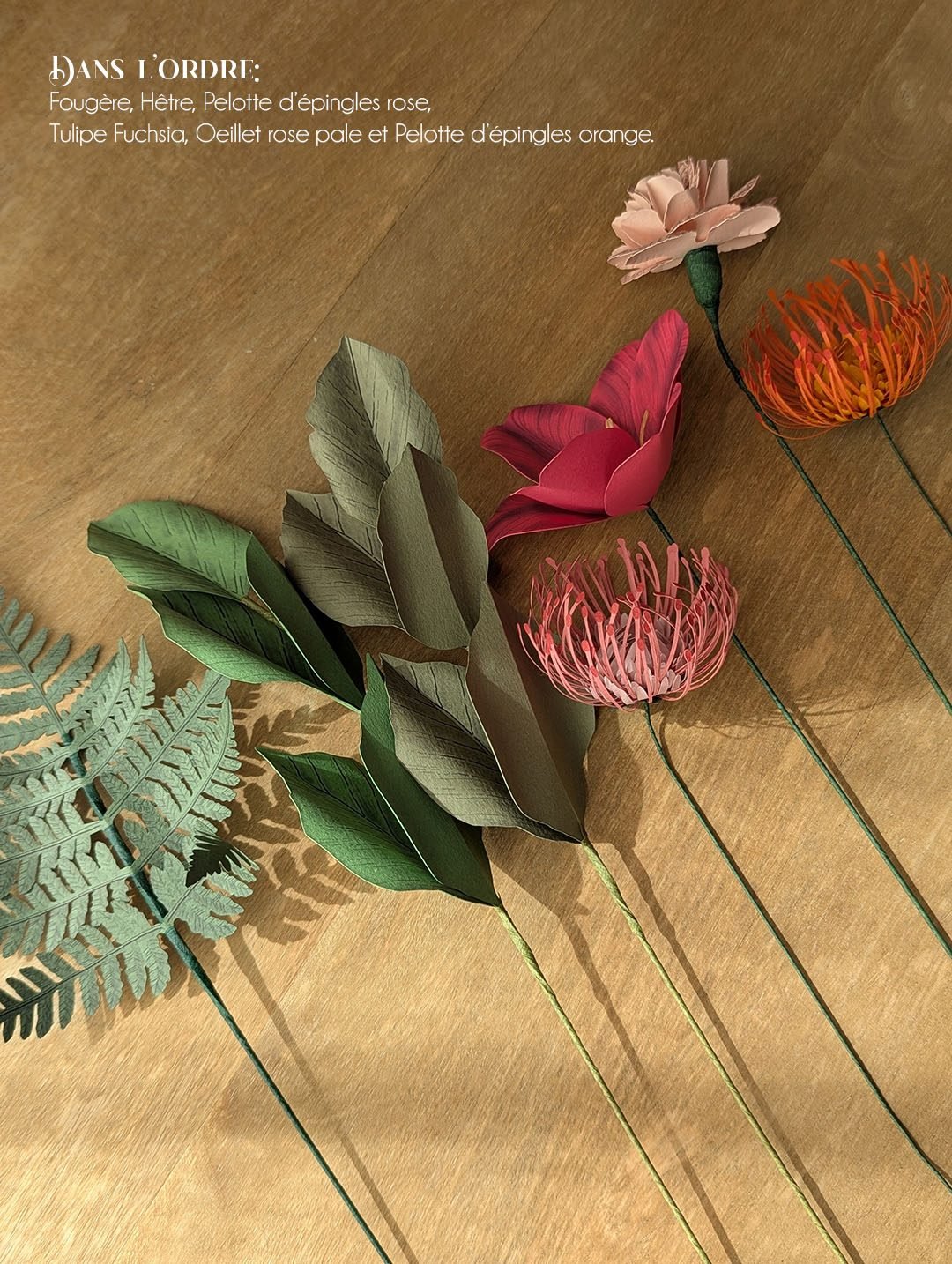 Sélection de fleurs et feuillages en papier posés sur bois, fougère, hêtre, tulipe fuchsia, oeillet et têtes d'épingles