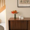 Bouquet de fleurs en papier orange dans un vase vert posé sur un buffet en noyer, à côté de deux pots en céramique blanche