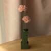 Deux oeillets en papier coloris Rosa dans un vase coloris vert sur une table en bois