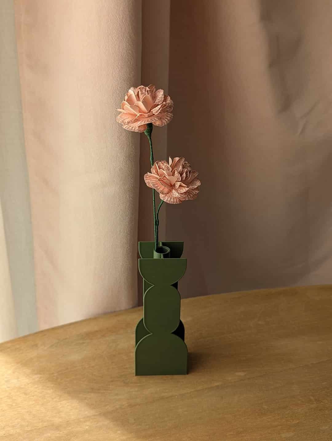 Deux oeillets en papier coloris Rosa dans un vase coloris vert sur une table en bois