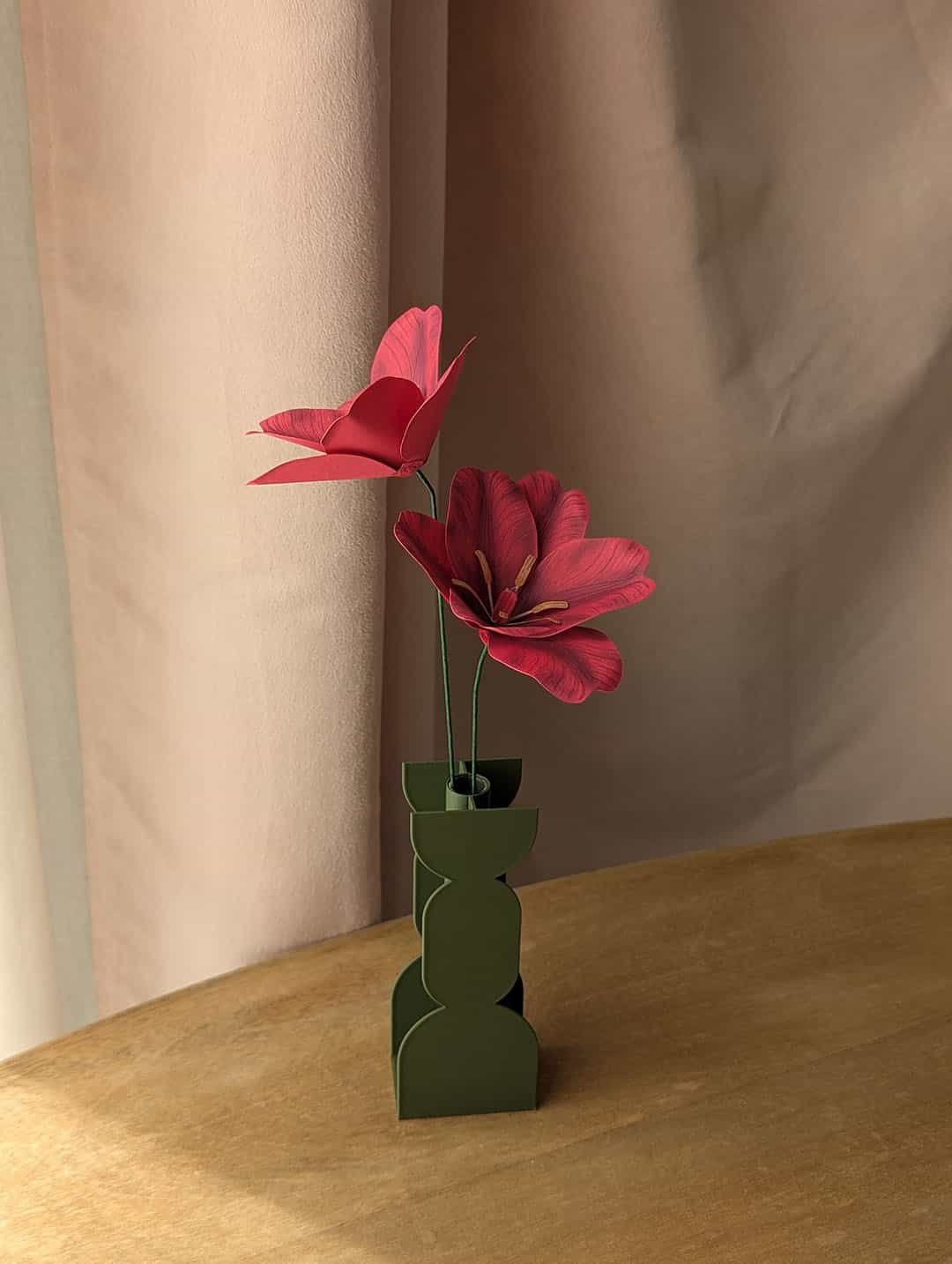 Deux tulipes ouvertes en papier fuchsia dans un vase coloris vert sur une table en bois